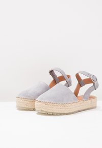 Šedé semišové espadrilky na korkovém podpatku, uzavřená špička a nastavitelné kotníkové pásky s kovovými detaily. Pletený jutový prvek.