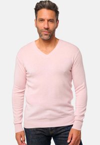 Pull à col en V rose clair en matériau tricoté doux, avec des manches longues et des poignets et un ourlet côtelés, associé à un jean en denim foncé.