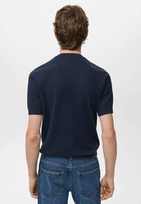 Polo a maniche corte in maglia a coste blu navy visto da dietro, con colletto a girocollo e texture liscia, abbinato a jeans blu.