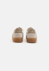 Beige sneakers with textured mesh and smooth suede sections, featuring a brown rubber sole and minimalistic design, viewed from the back.