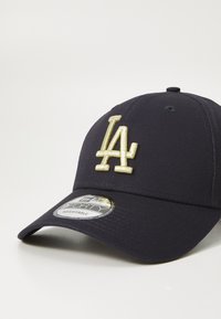 Jūras spēku beisbola cepure, izgatavota no auduma, ar zeltītu izšūtu "LA" logo priekšpusē, nedaudz izliekta viziera daļa un regulējama aizmugure.