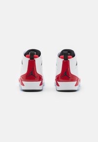 Zapatillas blancas con acentos rojos, diseño de caña alta, paneles texturizados, interior negro y logotipo visible. Suela transparente con patrón de tracción.