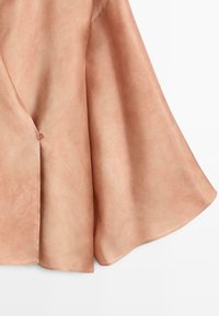 Weicher Wildlederstoff in hellbrauner Farbe mit sichtbarem Faltenwurf und einem kleinen Stoffschlaufen-Detail nahe am Rand.