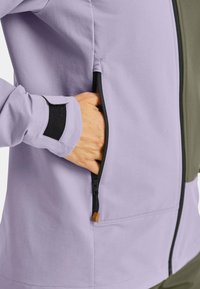 Light purple jacket with black zipper and pocket, featuring a textured fabric and velcro cuff detail. Part of jacket is olive green.