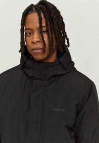 Black waterproof jacket made of textured fabric, featuring a high collar and a subtle logo on the chest. Classic straight cut design.