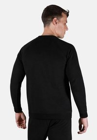 Sudadera negra de cuello redondo con mangas largas, puños y dobladillo acanalados. Textura suave, diseño minimalista y una etiqueta rectangular sencilla en la parte trasera.