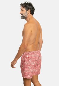 Bañador rojo con un patrón floral y acentos blancos, cinturilla elástica y bolsillos laterales, visto desde la parte posterior.