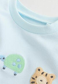 T-shirt en coton bleu clair avec une tortue verte brodée et un motif de tigre beige aux rayures noires et au nez rond.