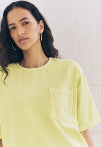 T-shirt in cotone di colore giallo chiaro con maniche corte, collo rotondo e tasca sul petto a sinistra. Tessuto liscio e design casual.