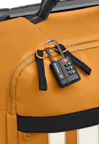 Borsa a duffle gialla in tessuto con superficie testurizzata, dotata di un lucchetto a combinazione nero e cuciture dettagliate lungo le cerniere e le cinghie.