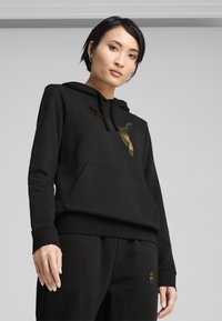 Black hoodie with a gold logo, features a kangaroo pocket, drawstring hood, and ribbed cuffs, paired with matching black pants.