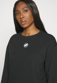 Sweatshirt noir à manches longues avec un col rond, arborant un logo animal blanc sur la poitrine. Le tissu semble doux avec une texture lisse.
