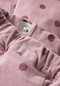 Roza somotna tkanina s većim bordo točkicama, sa naboranim elastičnim pojasom i detaljem bijelog dugmeta.