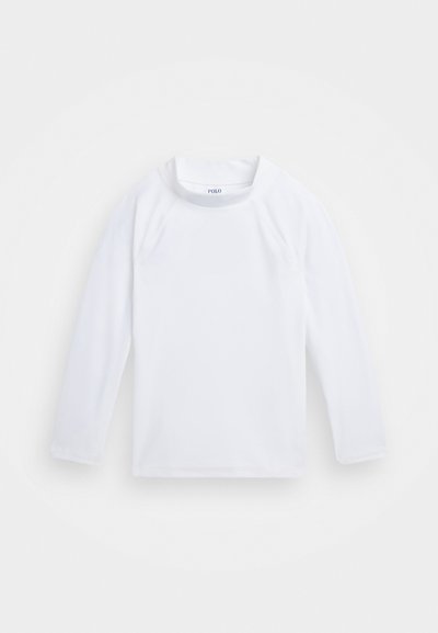 Camisa blanca de manga larga hecha de tejido suave. Presenta un cuello redondo y un discreto detalle de costura en las mangas y el dobladillo. Etiqueta con el logo visible.