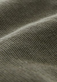 Primer plano de una tela de corduroy verde oliva arrugada que muestra finas estrías verticales y una textura suave.