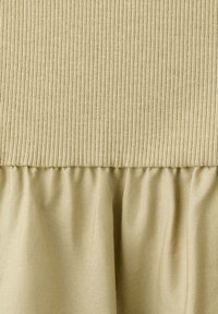 Tissu en maille côtelée beige passant à un tissu tissé beige lisse et froncé avec un contraste de texture visible.