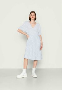 Vestido curto azul claro de mangas curtas com decote em V e pequeno padrão floral, apresentando uma cintura ajustada e saia rodada, combinado com botins brancos.
