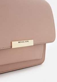 Borsa a tracolla in ecopelle rosa con un decorazione dorata che riporta la scritta "MICHAEL KORS", caratterizzata da bordi cuciti e una forma rettangolare ben definita.