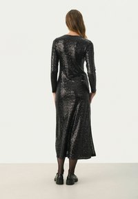 Robe longue noire à paillettes avec des manches longues et une silhouette ajustée, présentant une longueur mi-mollet et une texture lisse et brillante.
