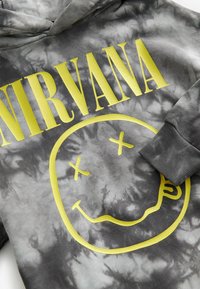 Šedá mikina s tie-dye vzorem a jasně žlutým nápisem "NIRVANA" doplněná grafikou usmívající se obličeje s kříženýma očima. Bavlněný materiál, volný střih.