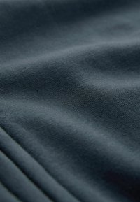 Tissu bleu foncé à texture lisse, présentant des plis subtils et des motifs fins en maille. Vue rapprochée mettant en avant la légèreté et la finesse du matériau.