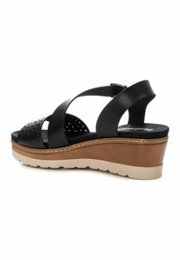 Sandalia de cuña de piel negra con parte superior perforada, diseño de correas cruzadas y suela en capas marrón y beige. Incluye correa ajustable para el tobillo.