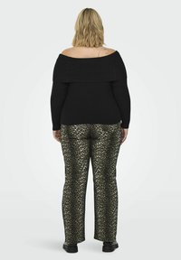 Zwart geribbelde off-the-shoulder trui gecombineerd met een broek met luipaardprint. De broek heeft een glanzende textuur en zwarte schoenen.