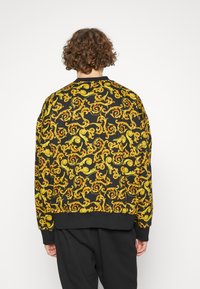 Sudadera negra con un patrón amarillo en espiral, cuello y puños acanalados, y un corte relajado. Tejido texturado con un diseño casual.