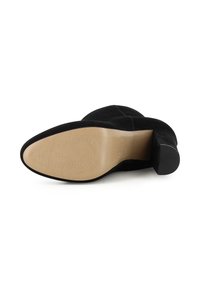 Zwarte suède enkelboots met een ronde neus, lage blokhak en een gladde beige rubberen zool. Bevat een lichte textuur op de zool.