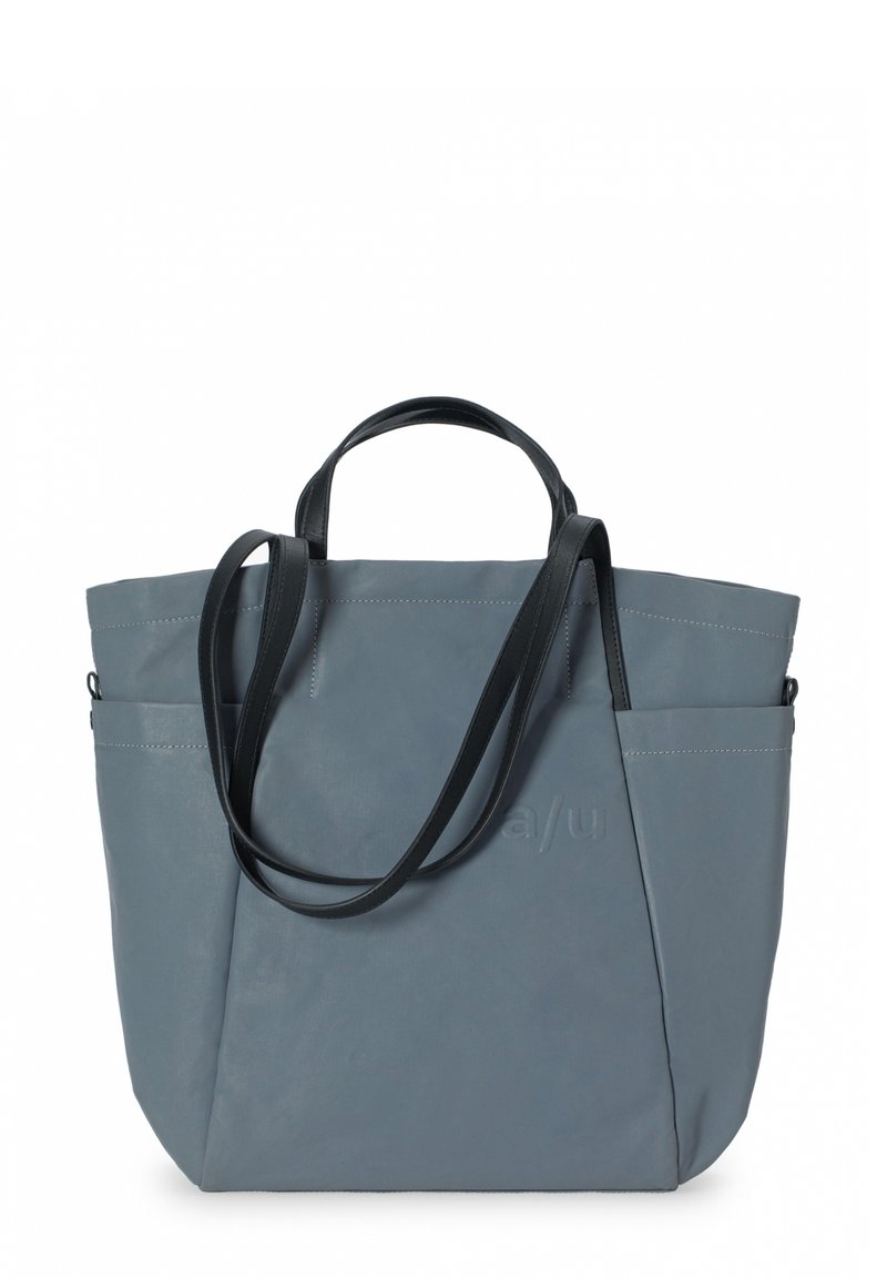 Grå tote taske lavet af glat materiale, med to sorte håndtag, sidelomme og syningsdetaljer. Minimalistisk design med logo accent.