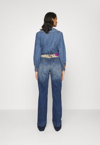 Jaqueta de ganga com uma cintura estampada em flores, apresentando mangas longas e gola, combinada com jeans de ganga de cintura alta e pernas largas.