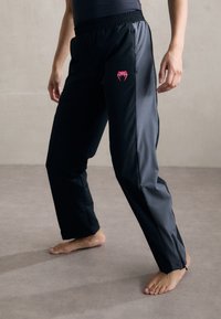Sorte treningsbukser med en rosa logo, med elastisk midjebånd og tapered bein. Glatt, lett materiale og glidelåsdetaljer.