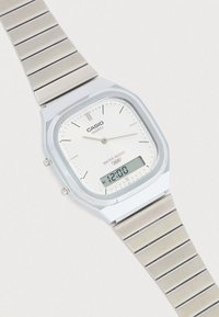 Ασημένιο ρολόι Casio quartz με μπρασελέ από ανοξείδωτο ατσάλι, ορθογώνιο καντράν, λευκό καντράν, μαύρους δείκτες ώρας και ψηφιακή οθόνη για το ξυπνητήρι.