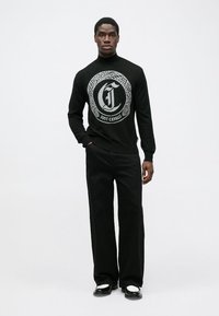 Pulover negru din tricot cu un design de logo argintiu, asortat cu pantaloni negri cu croi larg și pantofi negri cu accente albe.