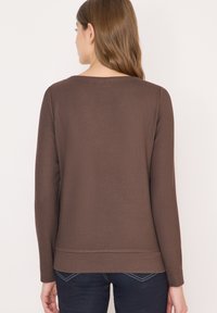 Hnědý žebrovaný svetr s dlouhým rukávem, volným střihem a širokým výstřihem, s lemem sahajícím pod pas. Hodí se k tmavým džínám.