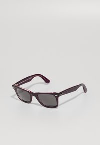 Tamno ljubičaste Ray-Ban Wayfarer sunčane naočale s crnim staklima, prikazane pod kutom na neutralnoj svijetloj pozadini.