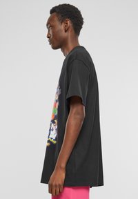 Sort bomulds T-shirt med et farverigt grafisk print på forsiden. Korte ærmer, afslappet pasform og slidser i siderne ved nederkanten.