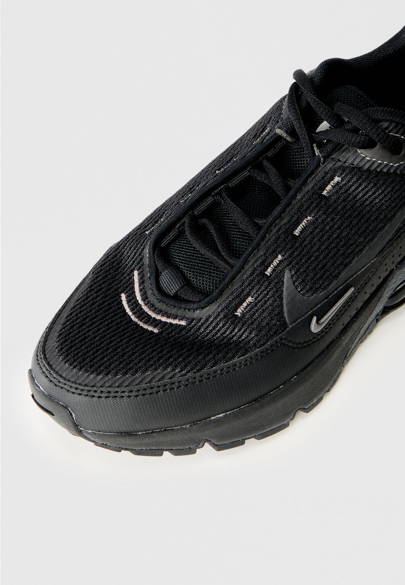 Zapatilla deportiva negra con upper texturizado, cierre con cordones y suela de goma lisa. Los acentos incluyen un sutil logo de swoosh y costuras en contraste.