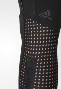 Mustat Adidas-legginssit, joissa on rei'itetyt verkkomateriaalit ja etuvetoketjuvalikoima valkoisella taustalla.