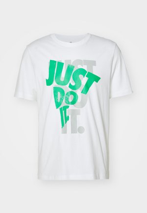 Camiseta blanca de algodón con gran texto verde "JUST DO IT" superpuesto sobre texto gris. Cuello redondo, mangas cortas, textura suave.