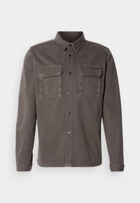 Chaqueta de camisa gris en mezcla de algodón con dos bolsillos en el pecho, frente con botones y cuello de pico; presenta mangas largas y un dobladillo recto.