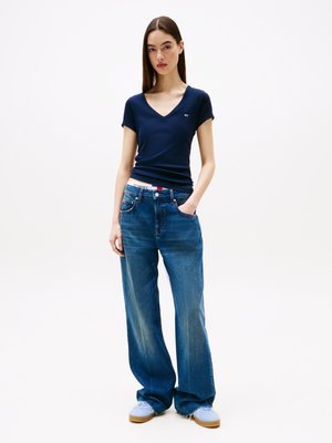 T-shirt bleu marine en V, fabriqué en tissu doux, associé à un jean ample clair avec une taille TOMMY et des baskets bleu clair.
