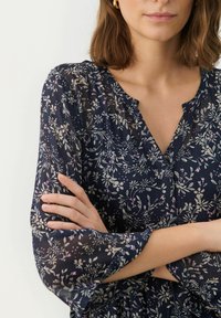 Bluză florală cu mâneci 3/4 transparente, decolteu în V, fundal bleumarin și modele botanice în roz deschis și crem. Material moale și ușor.