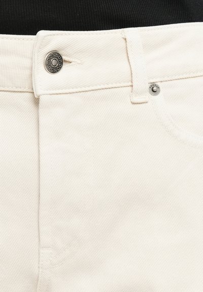 Plano detalle de la cintura de unos pantalones de mezclilla blanca con botón de metal y remaches grabados con "DONDUP".