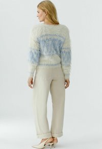 Pluizige trui met blauwe en witte strepen, lichte kleur, gecombineerd met beige omslagbroek en nude hoge hakken. Gladde textuur.