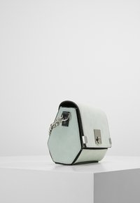 Sekskantet håndtaske i lys mintgrønt læder med en glat tekstur, sølvhardware og en kædestrop til at bære.