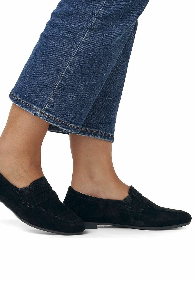 Scarpe slip-on in suede nero con tacco basso, caratterizzate da una fascia decorativa sul davanti e una texture liscia e opaca. Indossate con jeans cropped.