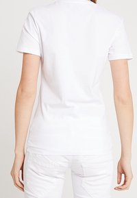 Biała bawełniana koszulka z krótkim rękawem, okrągłym dekoltem i dopasowanym krojem. Gładka tekstura z minimalną ilością szwów i bez widocznych grafik.