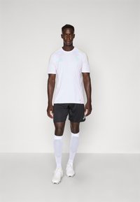 Hvit kortermet trøye med lyserøde og gule detaljer, sammen med svarte shorts og hvite knesokker. Hvite fotballsko.
