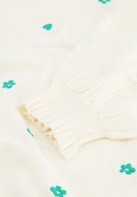 Maglione crema con fiori e motivi fogliari ricamati in turchese. Presenta una dettagliata manica arricciata e a costine per un finish testurizzato.